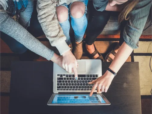 Three people sitting on a couch pointing at a laptop.